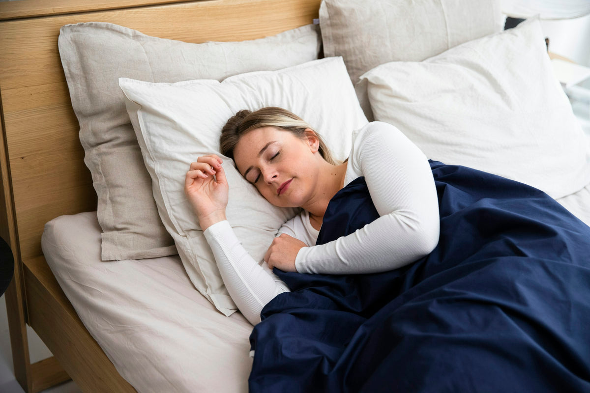 Woman asleep in a bed with white pillows and a navy blanket